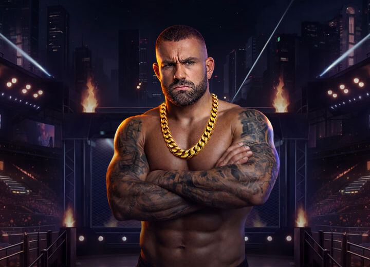 Muscular tattooed man with crossed arms and a thick gold chain stands inside a brightly lit arena, resembling an MMA cage.